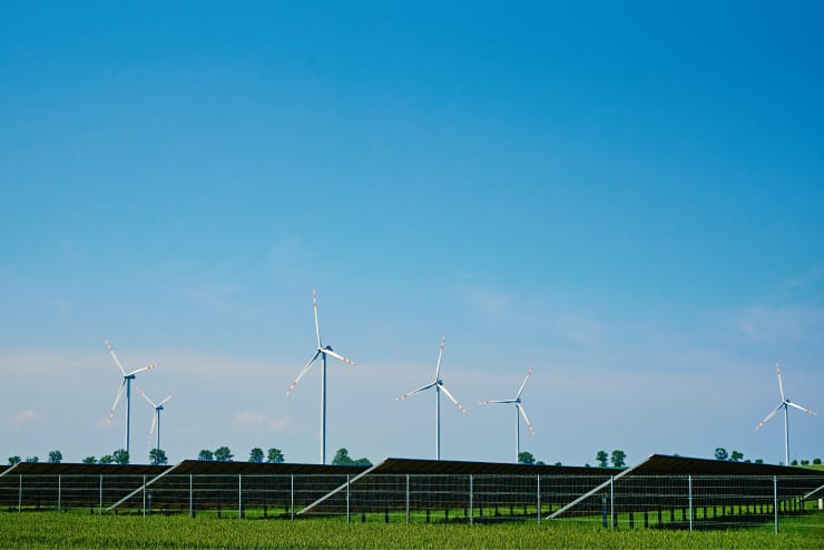 Wind turbines rising above a long solar array on open farmland under a clear blue sky